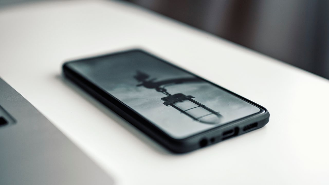 heros-img Close-up of a smartphone displaying a blurred image, placed on a desk beside a laptop.